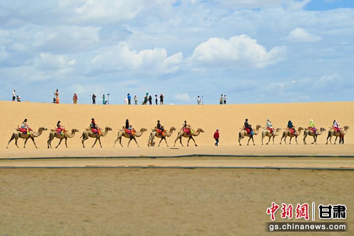 图为甘肃敦煌鸣沙山月牙泉景区内，游客在驼队旁进行旅拍。李亚龙 摄