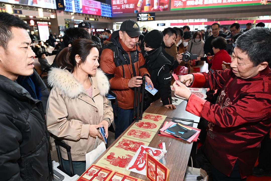 剪纸非遗传承人刘桂芝、冯元平等将一张张漂亮、吉祥的剪纸作品赠送给旅客。 记者 查金辉 摄